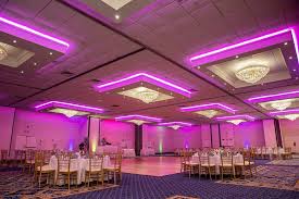 Elegant event space with round tables set for a wedding, featuring pink ambient lighting and decorative chandeliers, suitable for upcoming events hosted by Fresh New Angle Events.