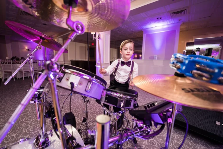 Little boy in a black bowtie and red suspenders, white shirt, playing drums at a wedding